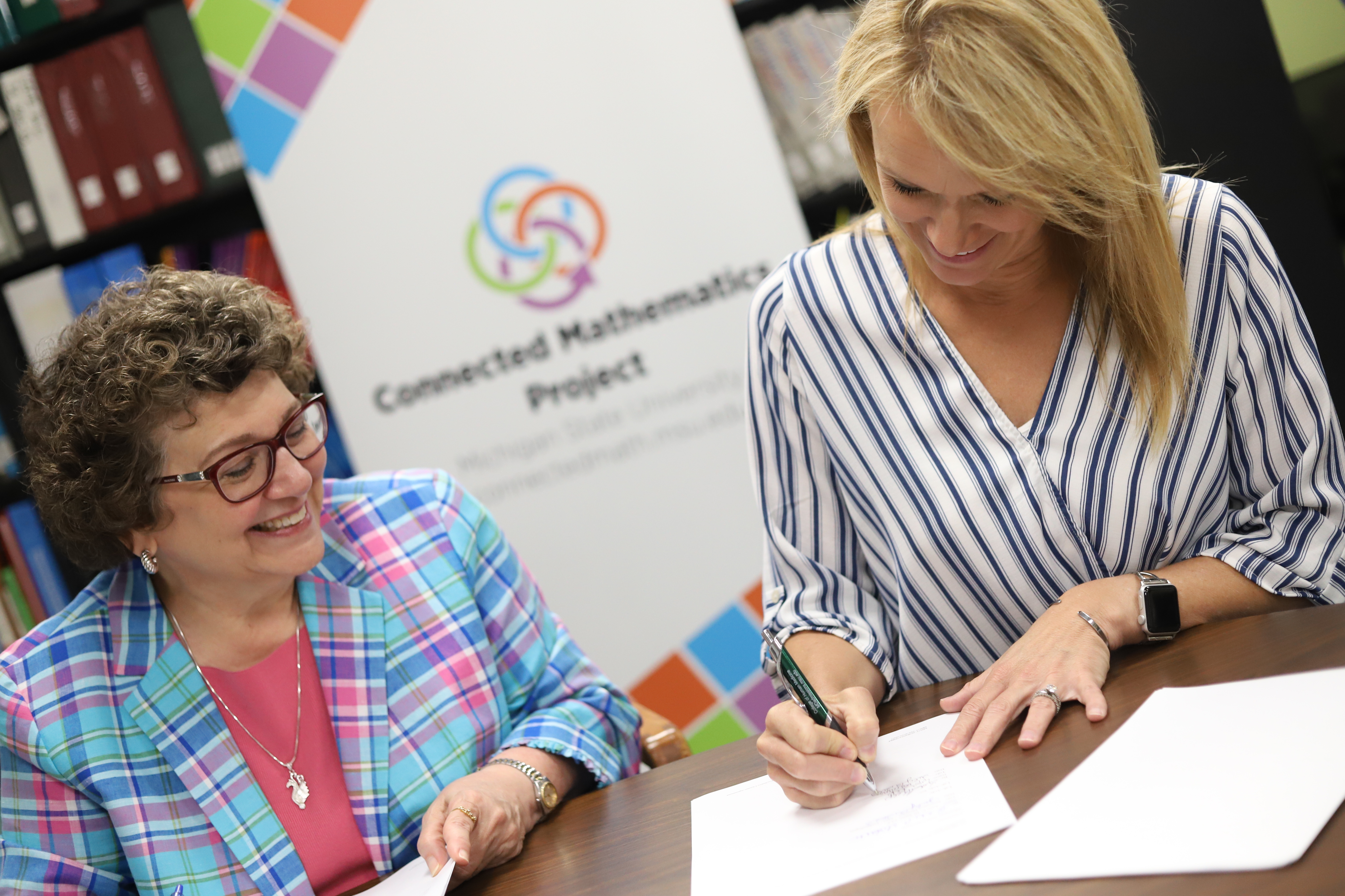 Anne Di Sante (left), Executive Director of MSU Technologies, and Lisa Kelp (right), VP of Learning and Development at Lab-Aids sign the partnership agreement for Lab-Aids to publish the next edition from Connected Mathematics Project at Michigan State University.
