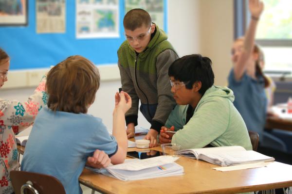 Busy science classroom - group of 4 in forefront discuss a plan